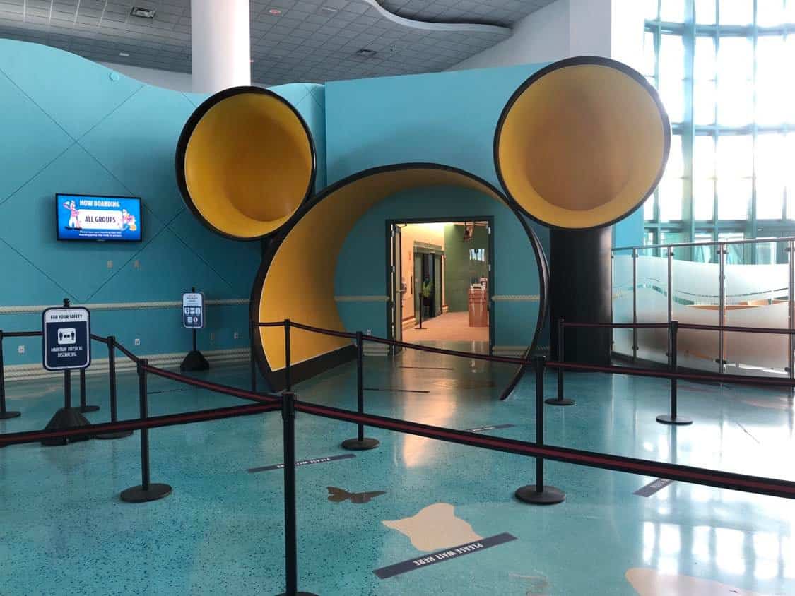 Mickey Mouse-shaped tunnel entrance with bright yellow ears welcomes Disney Cruise Line guests inside a lively indoor waiting area, capturing the magic and excitement of a Disney embarkation experience.