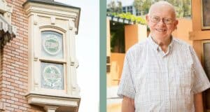 An iconic vintage sign adorns a brick building as Disney historian and archivist, wearing glasses and a plaid shirt, smiles warmly outdoors, evoking memories from the legendary Walt Disney Archives.