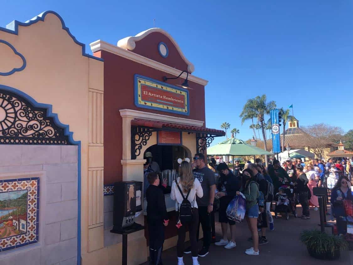 Guests line up under the sunshine at EPCOT’s El Artista Hambriento food booth, excited to taste Culinary Arts specialties during the International Festival of the Arts opening day.