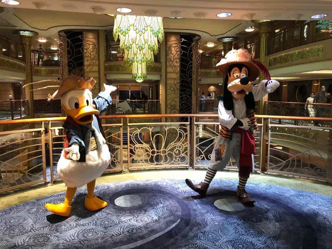 Donald Duck and Goofy, dressed in full pirate regalia, pose together on the deck of a Disney Cruise Line ship. The scene features elegant ship railings and warm lighting—capturing a magical character encounter that’s part of the unique Disney Cruise Line experience during Covid.