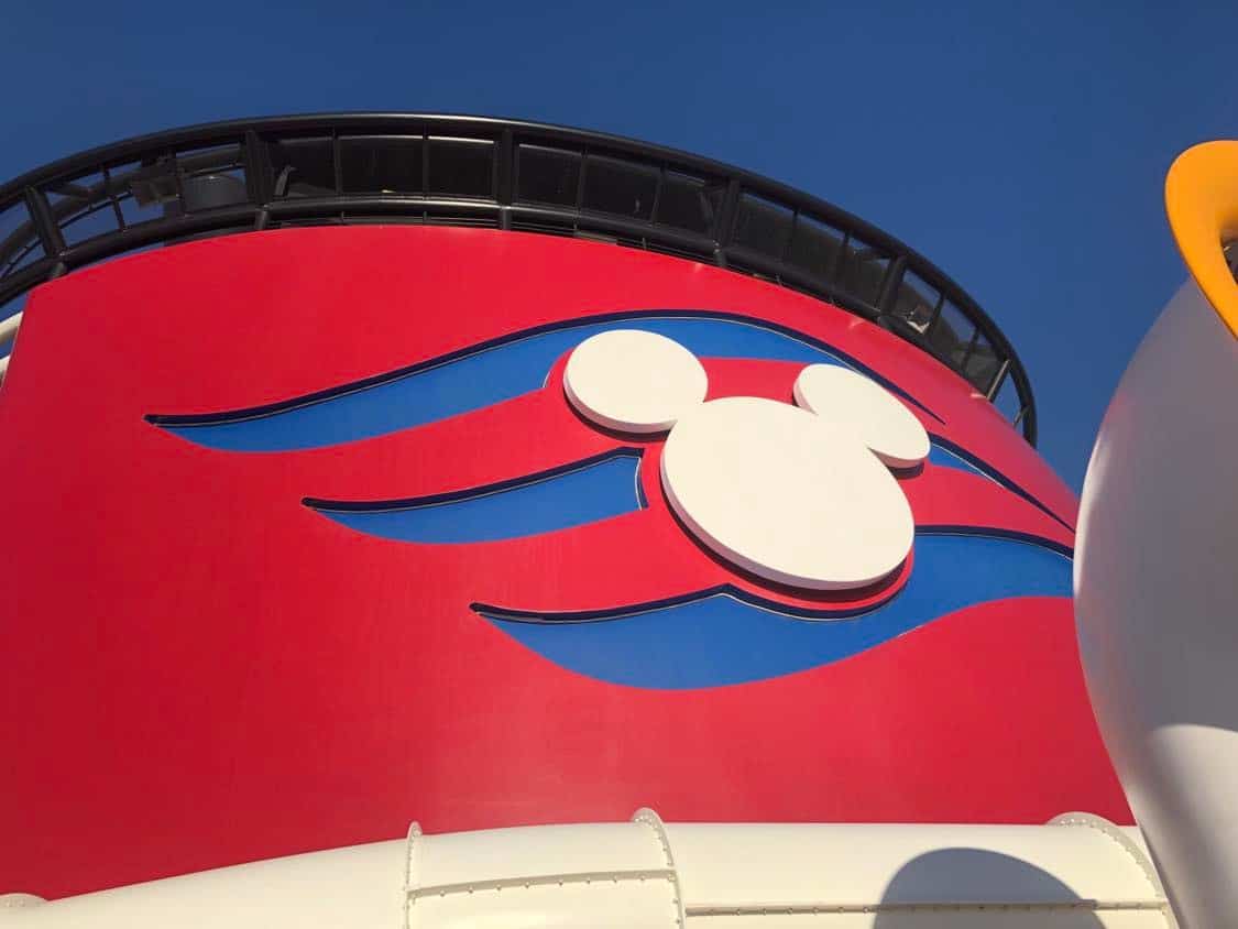 Iconic red funnel featuring the white Mickey Mouse logo and signature blue stripes rises against a vibrant blue sky on the deck of Disney Cruise Line, capturing the festive atmosphere of Pixar Day at Sea 2023—an unmissable celebration for Disney and Pixar fans.