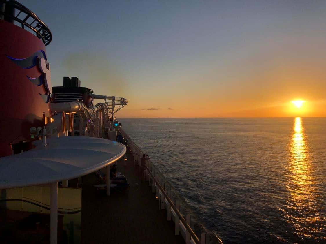 A breathtaking sunset seen from the deck of a Disney Cruise Line ship, where golden sunlight glimmers across the peaceful ocean—capturing the magic of Pixar Day at Sea 2023 for Disney fans and cruisers alike.