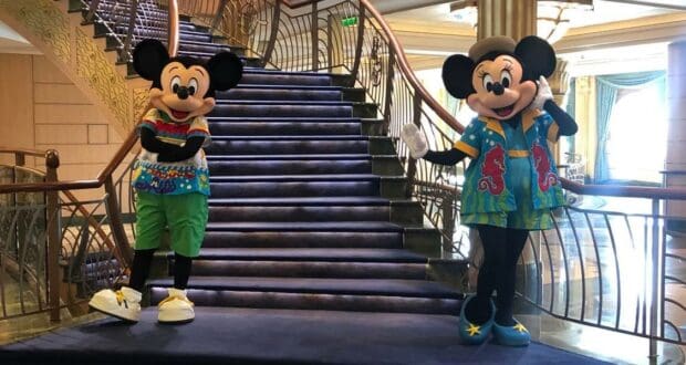 Mickey and Minnie Mouse dazzle in vibrant costumes as they pose together on a luxurious staircase with golden railings, bringing Disney magic to life aboard the cruise ship during My Disney Cruise Line Experience During Covid Part 3: Characters.
