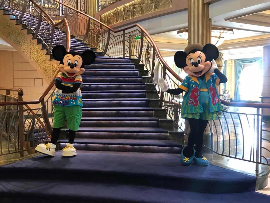 Mickey and Minnie Mouse dazzle in vibrant costumes as they pose together on a luxurious staircase with golden railings, bringing Disney magic to life aboard the cruise ship during My Disney Cruise Line Experience During Covid Part 3: Characters.
