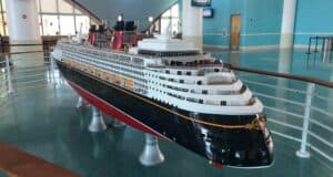 A showcase of a Disney Cruise Line ship model sits inside a themed exhibit with expansive windows and vibrant blue walls, reflecting Disney’s renowned attention to design detail and commitment to guest safety.