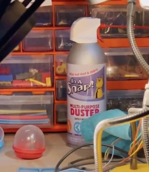 A can of multi-purpose duster sits on a desk cluttered with tools and tiny storage drawers, echoing the secretive workbench vibes you’d find behind the scenes at Avengers Campus.