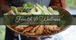 A guest enjoys a fresh bowl of salad with avocado and grilled chicken at Disney Springs. Text on image: Health & Wellness at Disney Springs.