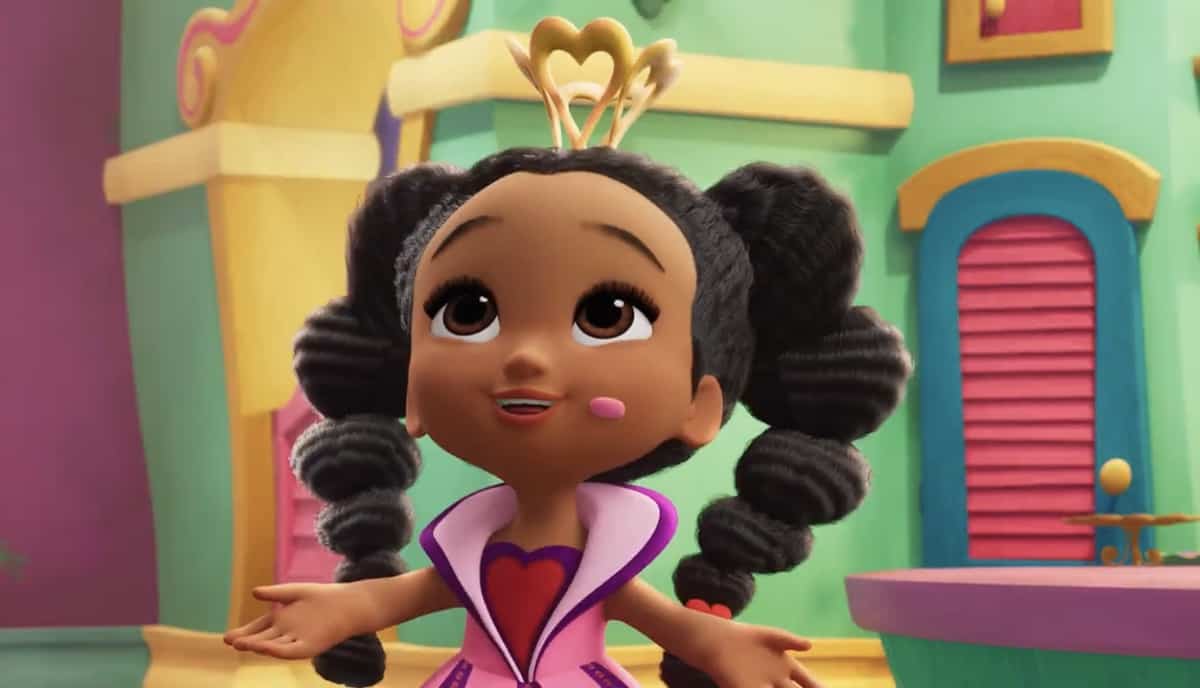 Alice from Alice’s Wonderland Bakery beams in her signature pink outfit with heart hairpin and playful pigtails, surrounded by a vibrant, storybook setting reminiscent of the whimsical world guests experience in the park attraction.