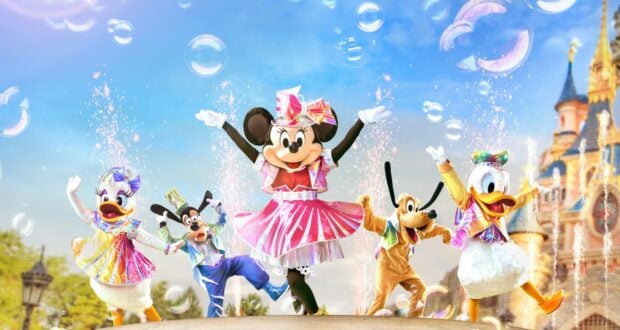 Minnie, Daisy, Goofy, Pluto, and Donald in vibrant costumes dance among floating bubbles in front of Sleeping Beauty Castle, celebrating the 30th Anniversary of Disneyland Paris.