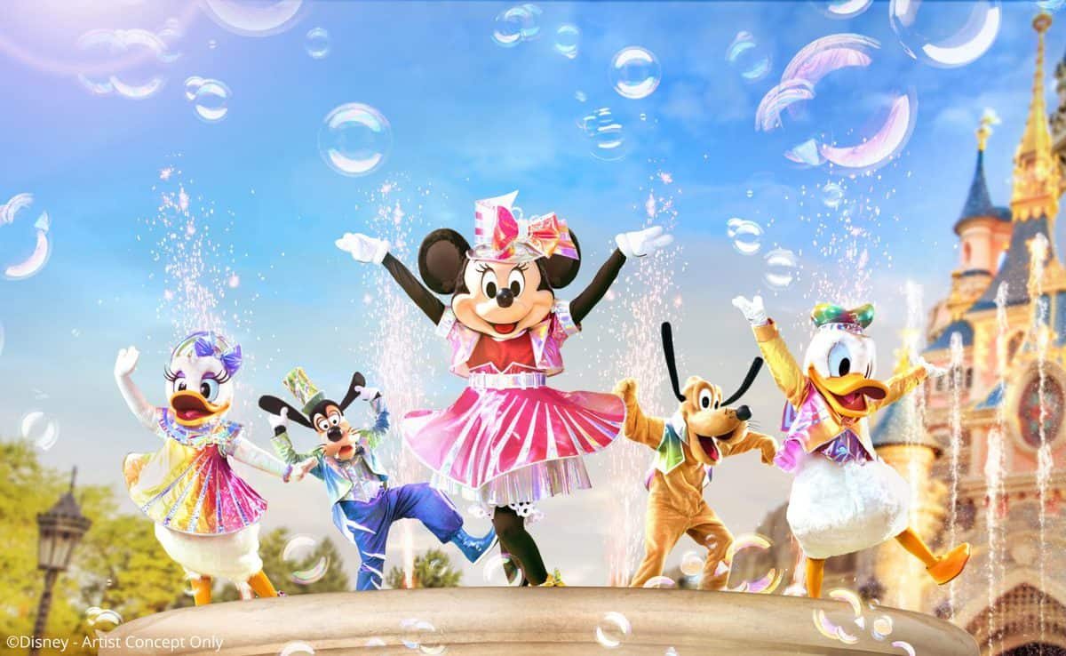 Minnie, Daisy, Goofy, Pluto, and Donald in vibrant costumes dance among floating bubbles in front of Sleeping Beauty Castle, celebrating the 30th Anniversary of Disneyland Paris.