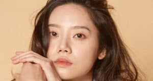 Kim Mi-soo, known for her star power on screen, stands with her signature long dark hair flowing as she smiles at fans, hands clasped near her face in a warm greeting, with the elegant beige backdrop giving a touch of classic Hollywood charm.