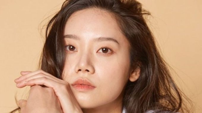 Kim Mi-soo, known for her star power on screen, stands with her signature long dark hair flowing as she smiles at fans, hands clasped near her face in a warm greeting, with the elegant beige backdrop giving a touch of classic Hollywood charm.