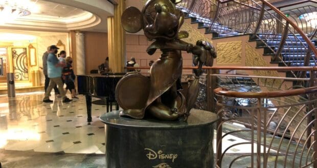 Mickey Mouse bronze statue dressed in a formal suit, welcoming guests in the grand lobby of the Disney Fantasy cruise ship, as featured in the My Disney Cruise Line Experience During Covid Part 5: Entertainment.