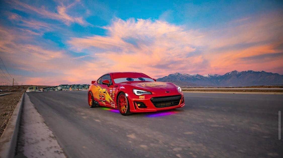 Lightning McQueen, glowing with neon lights and animated eyes, speeds along an open road at sunset with mountain vistas behind, just before a playful roadside twist—an iconic Cars moment brought to life for fans of Pixar’s Radiator Springs.