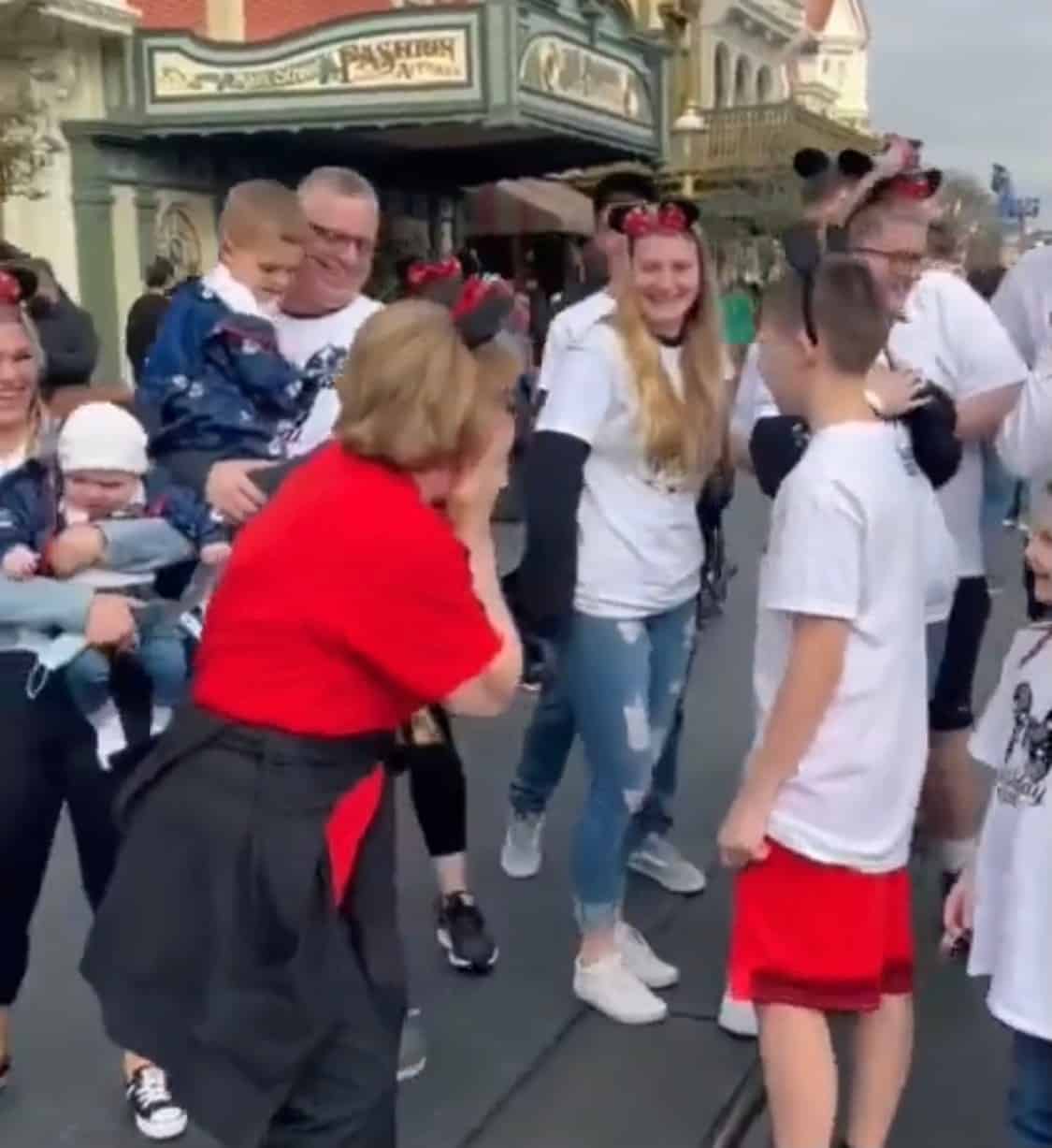 A joyful group beams and laughs on Main Street, U.S.A. in Disneyland, several proudly sporting Mickey Mouse ears. In this uplifting video, watch as a family pulls off an unforgettable 70th birthday surprise for their loved one right in the heart of the magic!.