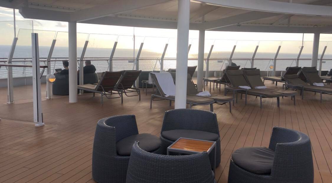 Tranquil outdoor deck on a Disney Cruise Line ship, featuring lounge chairs and tables positioned to offer panoramic ocean views at sunset; the mostly empty space evokes the relaxing adult-only areas highlighted in cruise experiences, providing guests with a peaceful retreat from the excitement of family entertainment onboard.