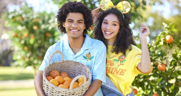 Festival-goers pose with a basket of oranges in front of lush orange trees, sporting playful citrus-themed shirts and headbands—a festive preview of exclusive merchandise coming to this year’s Citrus Festival.