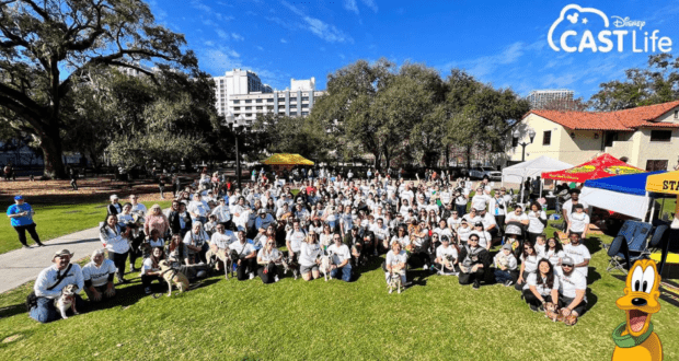 Disney fans and their dogs gather on the grass beneath a clear, sunny sky, joyfully celebrating as Disney CAST Life helps raise thousands for animals in need; Disney CAST Life logo appears in the corner.