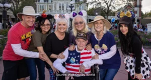 A joyful group of adults and a WWII veteran in a wheelchair, all sporting classic Mickey Mouse ears, gather for a special 100th birthday photo at Walt Disney World, surrounded by the park’s festive atmosphere.