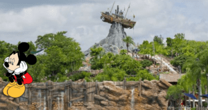 Mickey Mouse looks downcast in front of Disney World's water park, featuring a dramatic shipwreck perched on a rocky mountain surrounded by lush green trees, as the park remains closed for the fifth consecutive day.