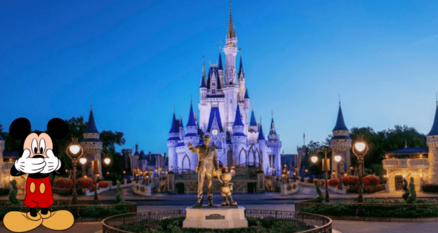 Mickey Mouse stands near Cinderella Castle at Disney World as the area is evacuated due to fire alarms, with a statue nearby and the park glowing with lights at sunset.