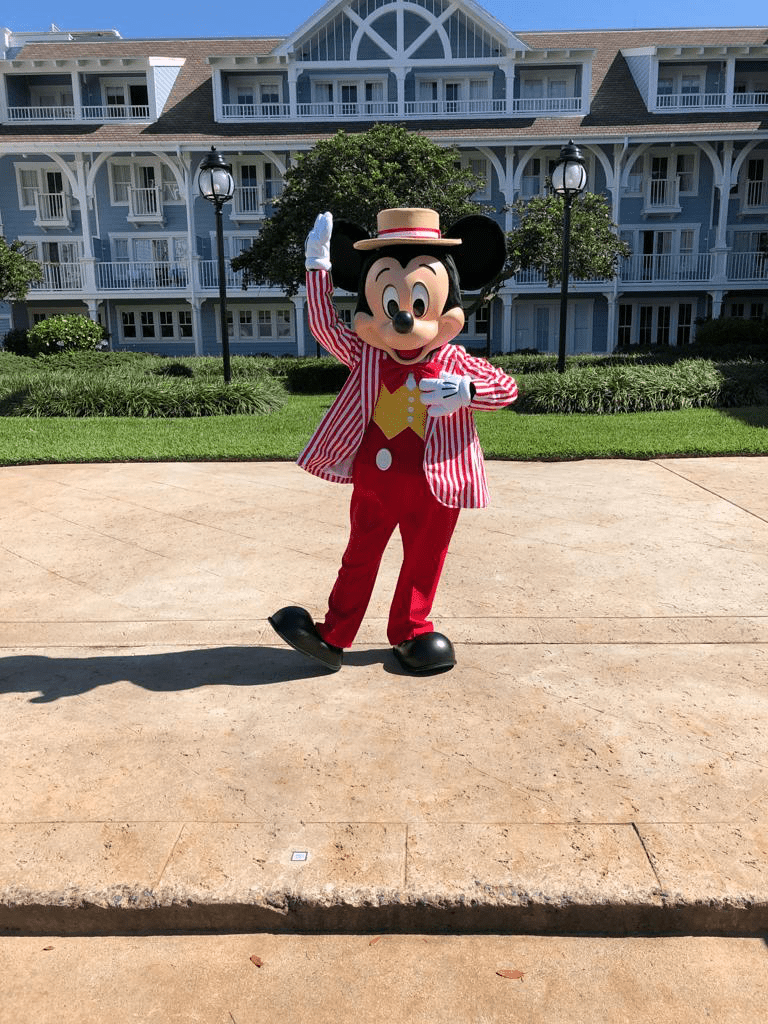 Mickey Mouse strikes a cheerful pose outside a large, blue building at Walt Disney World.