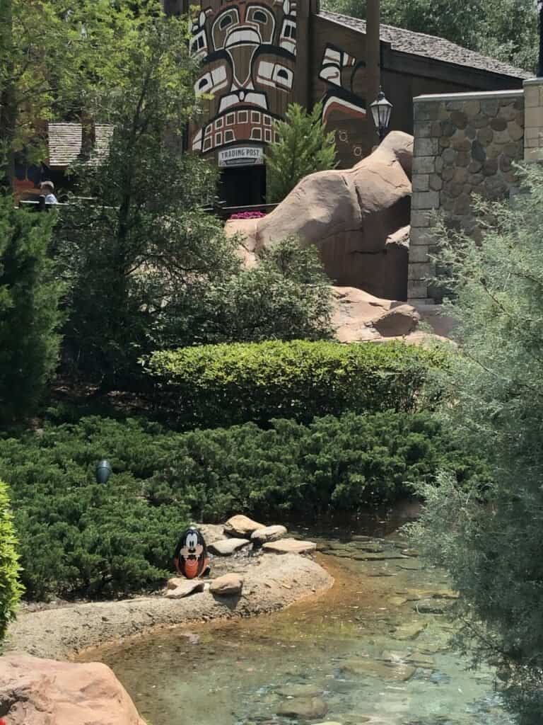 Goofy stands as a colorful cutout beside a scenic pond, surrounded by lush greenery and the iconic totem art building in the background, bringing extra Easter cheer to Walt Disney World for Disney Parks guests.