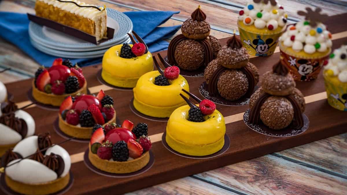 A tempting selection of vibrant pastries and cupcakes set out on a wooden tray atop a rustic table, capturing the magical dessert displays found across the Disney Skyliner Resorts.