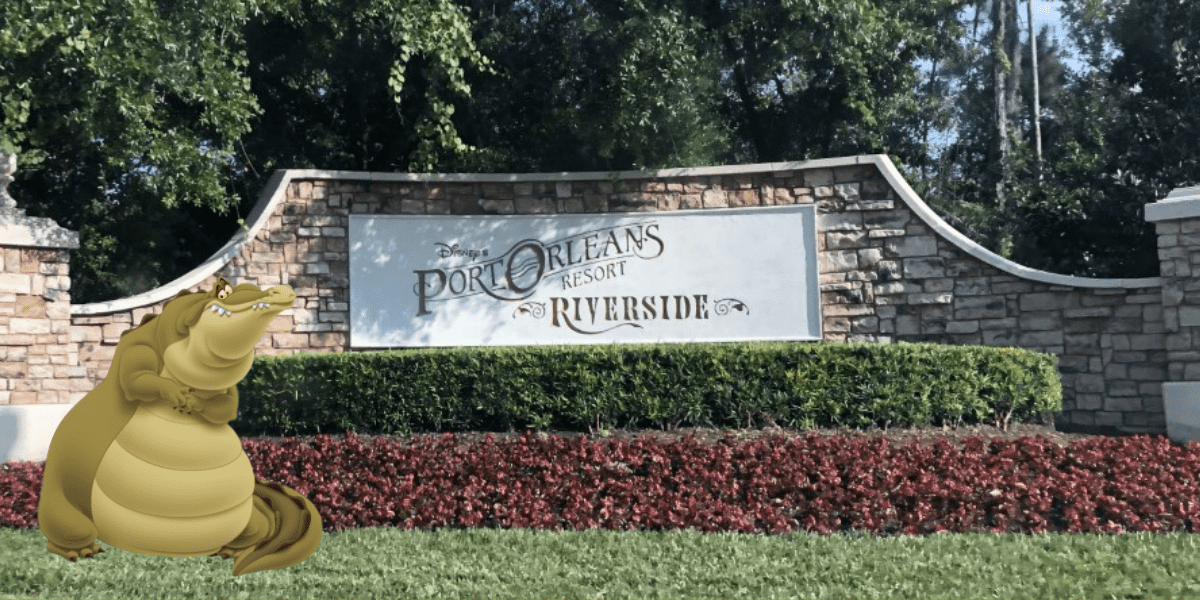 Louis the alligator greets guests with a big smile on the lush lawn in front of the iconic Port Orleans Resort Riverside entrance sign, setting a welcoming tone at this beloved Disney Resort.