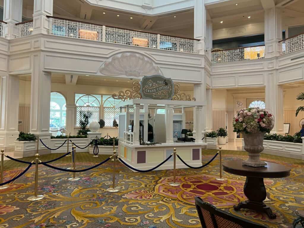 Grand lobby gleaming with elegant white decor, vibrant flower centerpiece, and a Disney Guest Services kiosk roped off in the middle—evoking the magical welcome and immersive atmosphere that Disney World resort fans know and love.