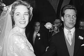 A bride and groom, dressed in classic wedding attire, share a joyful moment posing together during their special day. Amidst the festive spirit reminiscent of a Main Street parade at Disney World, there’s also a gentle note of reflection as guests learn of renowned Broadway set designer Tony Walton’s passing at age 87.
