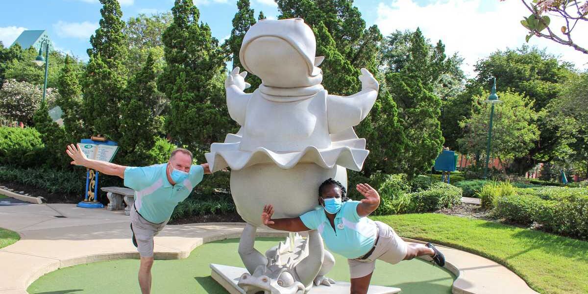 Guests in face masks strike a playful pose beside the iconic frog statue at Fantasia Gardens, each balancing on one leg and adding to the whimsical park atmosphere.