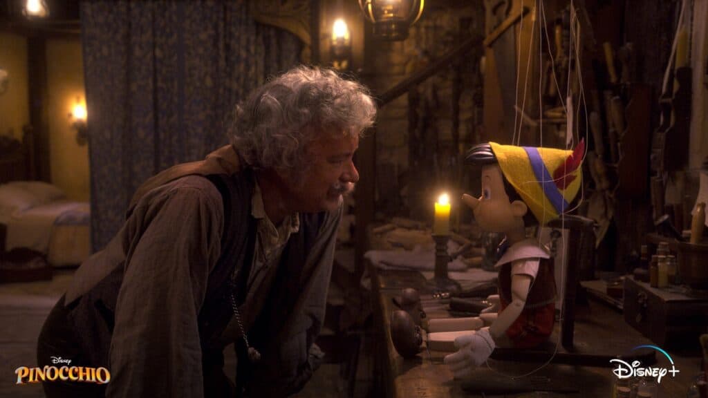 Geppetto, played by Tom Hanks, bends over his workbench in a warmly lit workshop to chat with Pinocchio, capturing the classic Disney magic of their heartfelt bond.