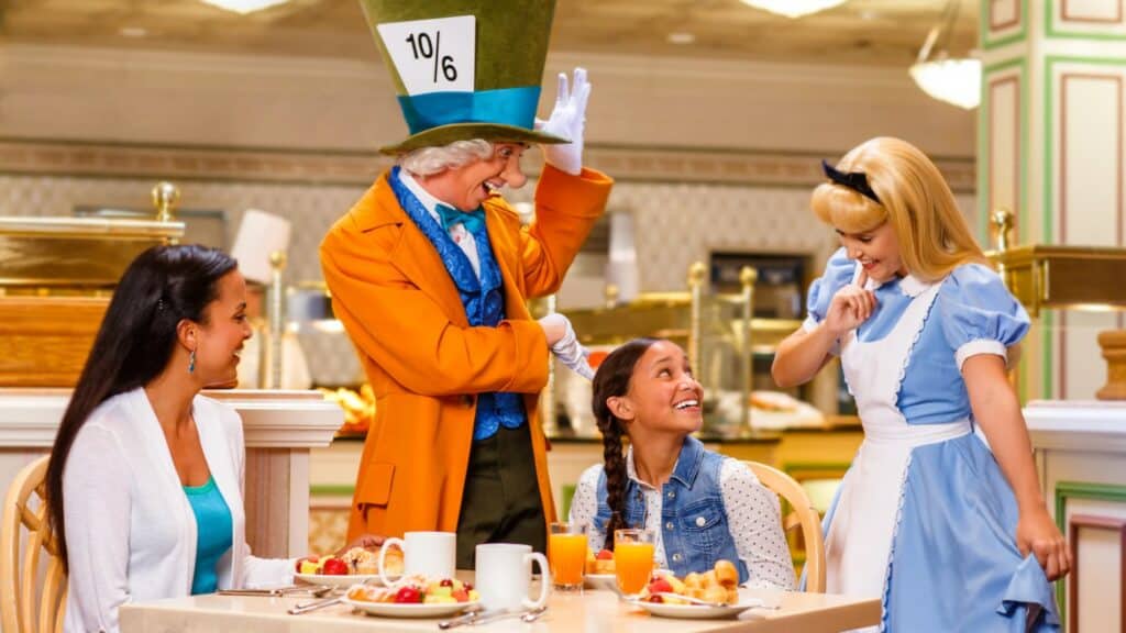 Two young guests beam with excitement as they share a breakfast table with Alice and the Mad Hatter at a Disney character dining experience, evoking the enchanting pre-COVID moments once found in Disney parks.