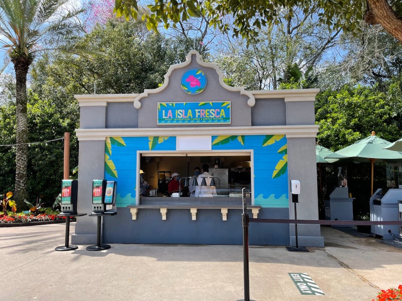La Isla Fresca at EPCOT beckons breakfast crowds with its lively, Caribbean-inspired booth, splashed in bold colors and framed by lush trees, while eye-catching drink dispensers promise a refreshing start to your park day.