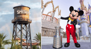 Mickey Mouse poses next to the Stanley Cup trophy in front of a Disney Springs water tower and a grand castle, all beneath a bright blue sky.