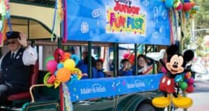 Mickey Mouse leads a vibrant Disney Junior Fun Fest parade float, surrounded by waving fans and bright balloons, spreading Disneyland magic and celebrating the dreams being fulfilled through Make-A-Wish.
