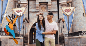 A cheerful couple stands at the iconic Sleeping Beauty Castle entrance, with Goofy enthusiastically waving nearby, embodying the unforgettable magic and thrills California residents can enjoy with special Disneyland tickets.