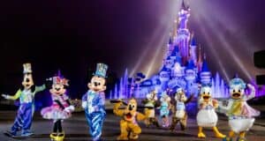 Beloved Disney characters like Mickey, Minnie, and Goofy gather in their vibrant costumes before Cinderella Castle, illuminated in dazzling lights and dramatic spotlights during the magical Disney EARidescent Event at Walt Disney World.