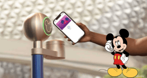 A guest scans their fully charged phone at a Walt Disney World park entrance, ready for a magical day, as Mickey Mouse enthusiastically waves nearby.