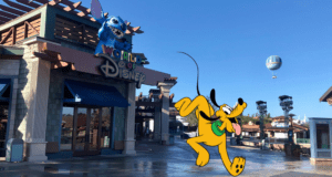 The iconic World of Disney store featuring Stitch perched mischievously above the entrance, while Pluto dashes by in true runDisney spirit. A festive balloon floats overhead, capturing the magic of Disney Springs.