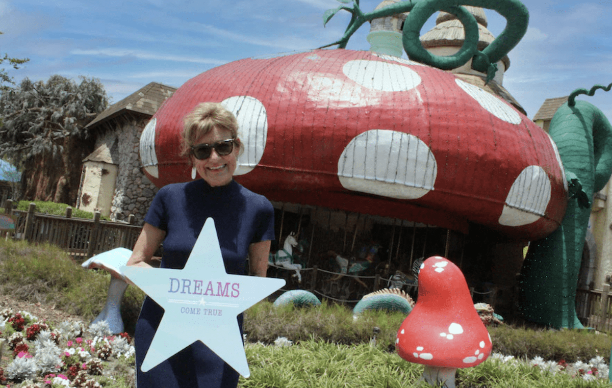 A guest holds a star-shaped sign reading "DREAMS COME TRUE" in front of the iconic giant mushroom at Give Kids the World Village, where magic and Disney donations help create unforgettable experiences for children and their families.