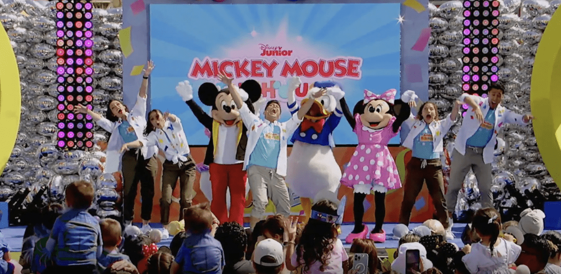 Mickey Mouse, Minnie Mouse, Donald Duck, and other Disney characters light up the stage at Disneyland, entertaining an excited crowd of children during a special Make-A-Wish event.
