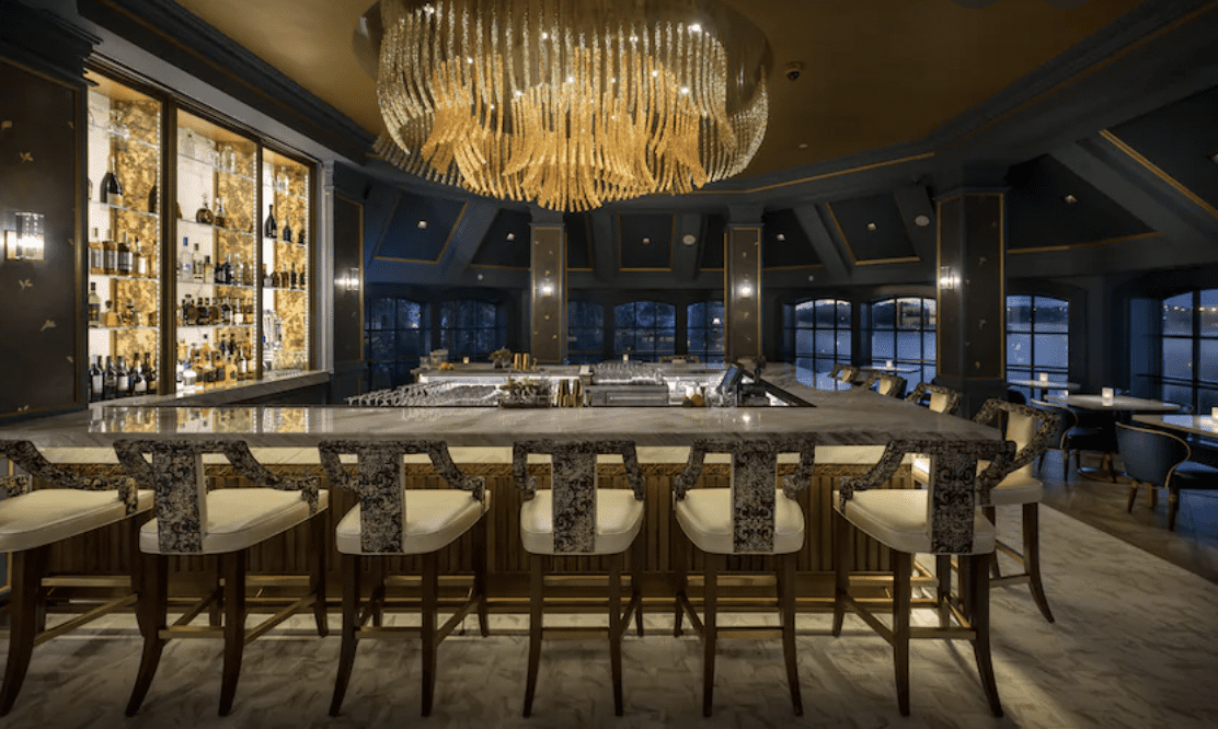 Upscale lounge at Disney’s Contemporary Resort featuring a sleek marble bar, eye-catching patterned chairs, a sparkling chandelier, and impressive bottle displays—an inviting spot to kick off your Monorail Bar Crawl in signature Disney style under atmospheric lighting.