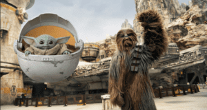 Chewbacca greets guests with a wave while Grogu floats alongside in his pod, set against the stunning sci-fi vistas of Star Wars: Galaxy’s Edge, bringing the adventure and magic of this Disney park to life.