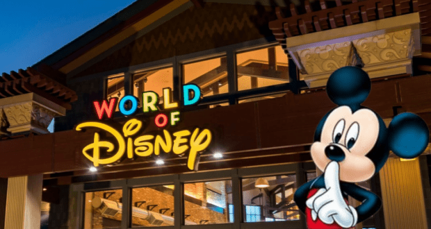The image features the illuminated exterior of the World of Disney store at Disney Springs, with a sign above the entrance. In the foreground, a large image of Mickey Mouse playfully holds a finger to his lips, set against a dusky sky—a perfect scene for Disney shopping enthusiasts.