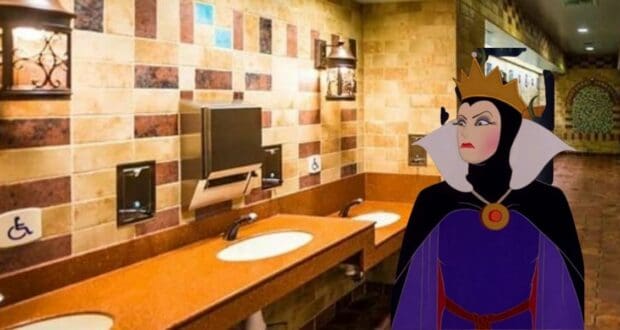 The Evil Queen from Disney’s Snow White, wearing her regal crown, stands in a brightly tiled restroom at the park, looking unimpressed as she seems to question why there are no mirrors at Disney World.