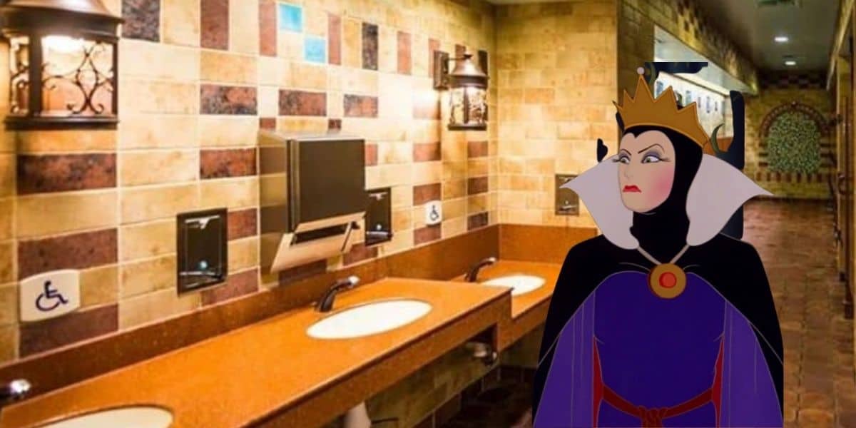 The Evil Queen from Disney’s Snow White, wearing her regal crown, stands in a brightly tiled restroom at the park, looking unimpressed as she seems to question why there are no mirrors at Disney World.