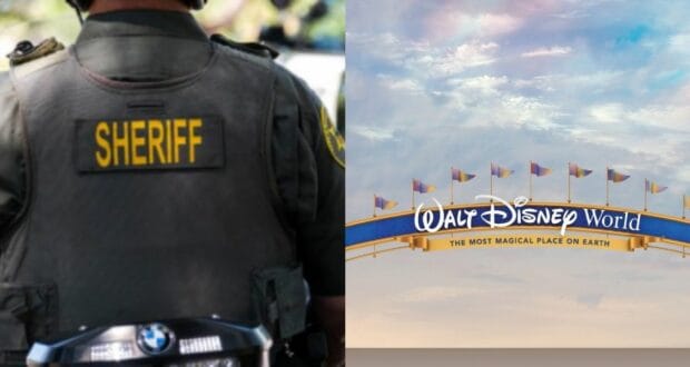 A sheriff stands near the iconic Walt Disney World entrance sign, facing away from the camera as colorful flags wave in the sunshine against a clear blue sky.