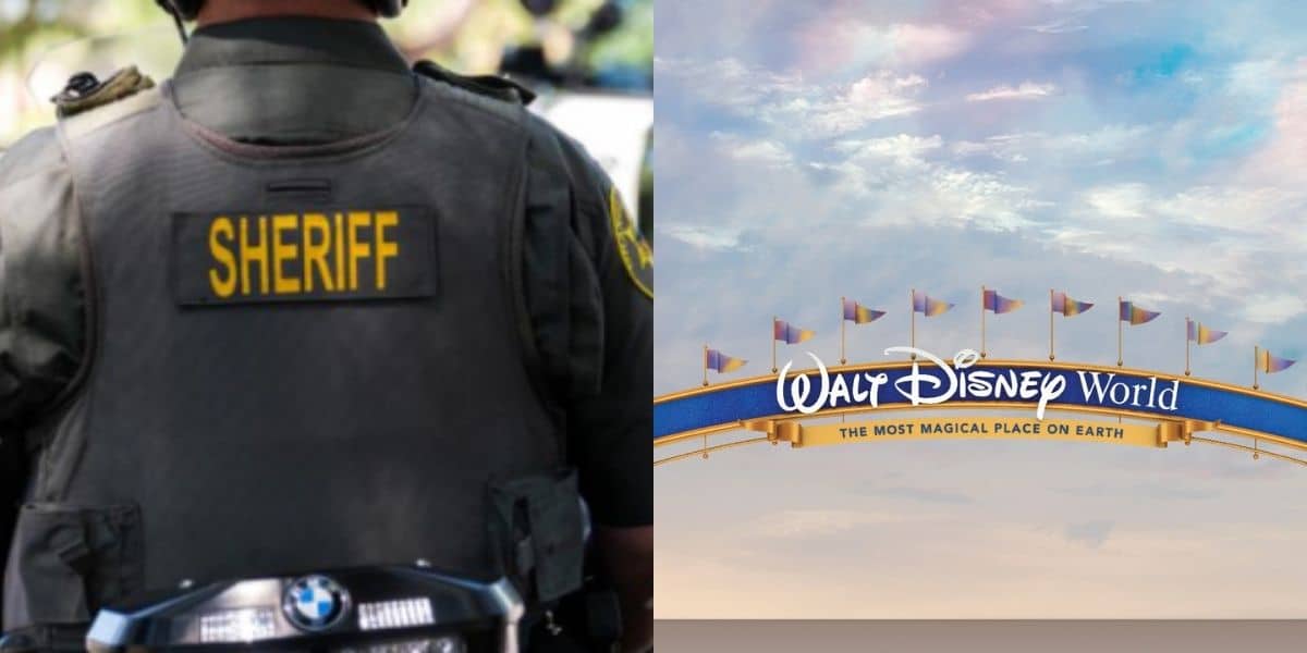A sheriff stands near the iconic Walt Disney World entrance sign, facing away from the camera as colorful flags wave in the sunshine against a clear blue sky.